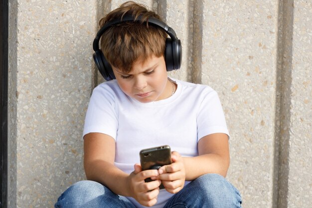 Menino em fones de ouvido com smartphone ouve música no parque