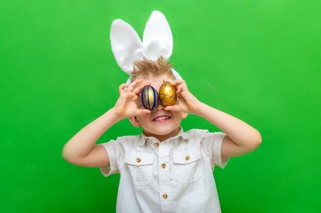 Menino em orelhas de coelho coelho na cabeça segurando ovos de Páscoa nos olhos em verde