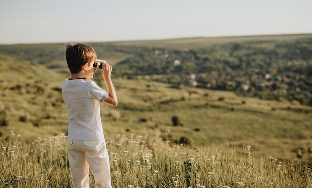 Menino em pé na colina verde olhando com binóculos