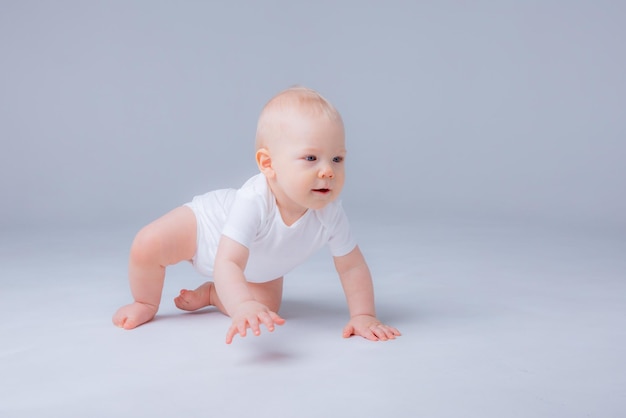 Menino em uma roupa branca rastejando em um fundo branco