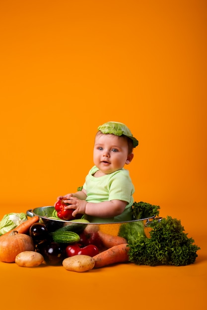 Menino em uma roupa verde senta-se em uma tigela de metal com legumes. conceito de produto agrícola