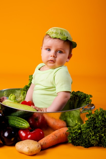 Menino em uma roupa verde senta-se em uma tigela de metal com legumes. conceito de produto agrícola