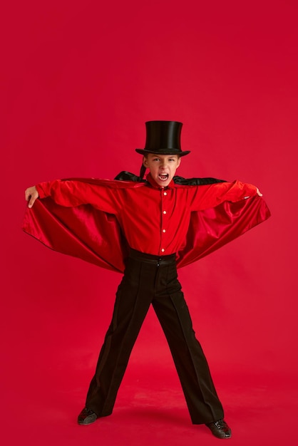 Menino emocional vestindo traje para a festa de Halloween da escola posando contra o estúdio vermelho