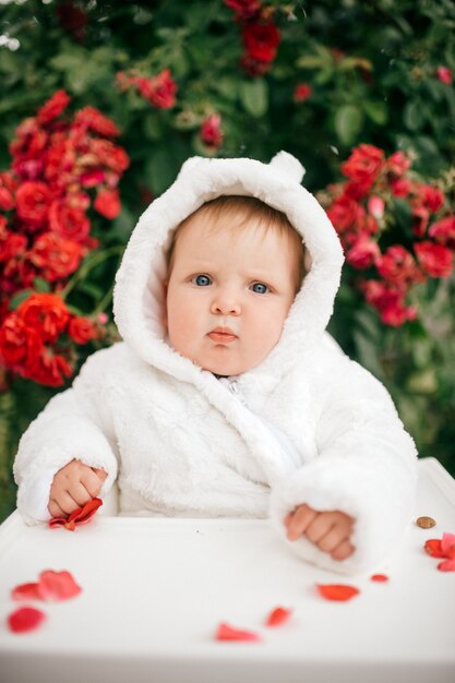 Foto menino encantador, sentado na cadeira alta ao ar livre nos arbustos com flores