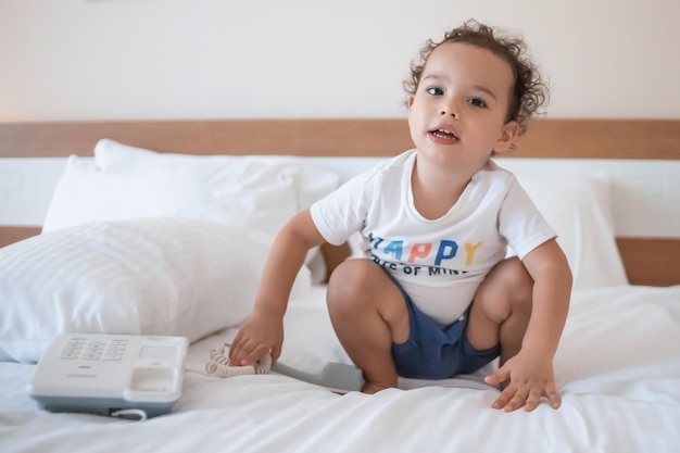 Foto menino encaracolado da criança que joga com um telefone com fio na cama