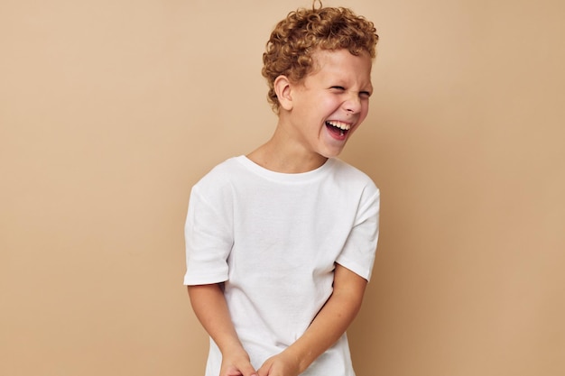 Menino encaracolado em uma camiseta branca posando fundo bege divertido