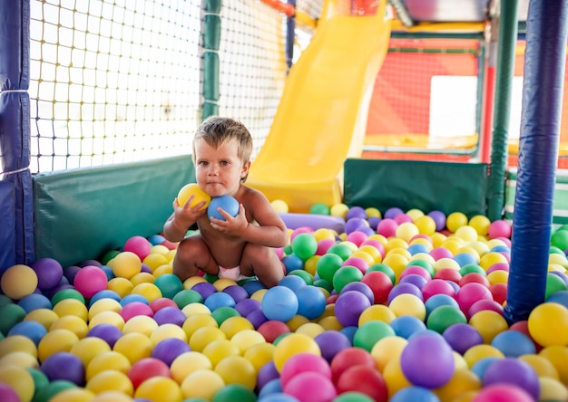 Menino engraçado alegre em uma fralda com uma bola listrada verde inflável nas mãos está jogando na sala de jogos no fim de semana desfrutando de dias quentes de verão brilhantes