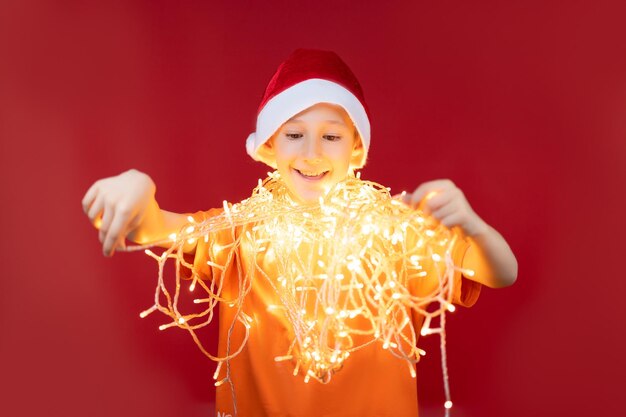 Menino engraçado com chapéu de Papai Noel, com uma guirlanda luminosa no pescoço