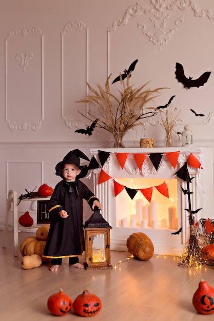 Foto menino engraçado com fantasia de bruxa de halloween com jack abóbora e vassoura dentro de casa