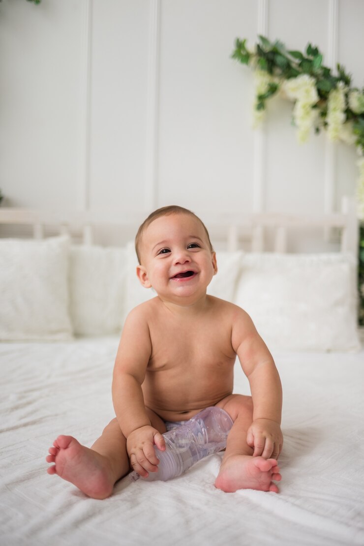 Foto menino engraçado de fralda sentado na cama segurando uma garrafa de água