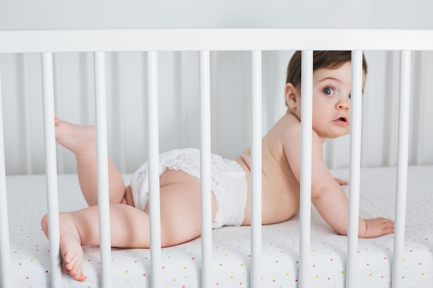 Menino engraçado deitado na cama de bebê com expressão de choque