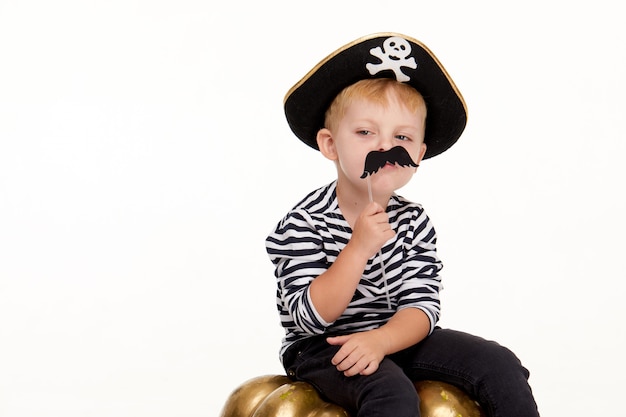 Foto menino engraçado em fantasias de carnaval de piratas em pé com uma grande abóbora em branco