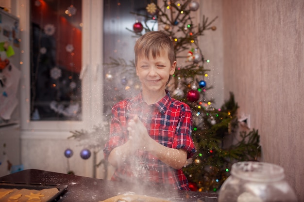 Menino engraçado está preparando o biscoito, assar biscoitos na cozinha de natal.