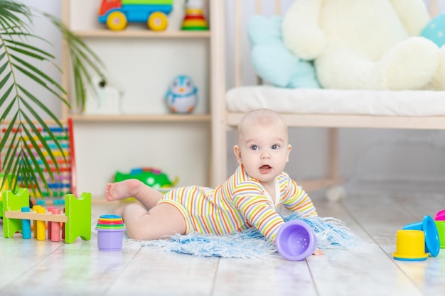 Menino entre os brinquedos no quarto infantil fofo, engraçado, sorridente, bebezinho brincando no chão, o conceito de desenvolvimento infantil e jogos