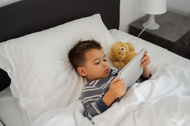 Menino envolvido em tecnologia de tablet na cama