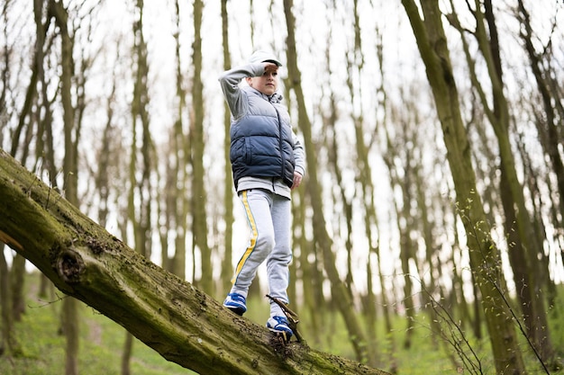 Menino escalou uma árvore derrubada na floresta de primavera Momentos felizes da infância