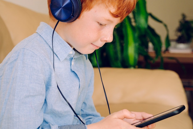 Menino esperto ouvindo música com fones de ouvido à prova de som do telefone móvel em casa.