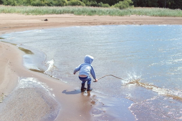 Menino espirrando água no rio com uma vara