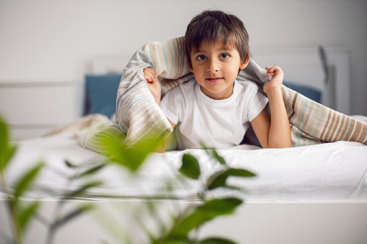 Foto menino está deitado na cama sob o cobertor listrado e não quer dormir, insônia e diversão