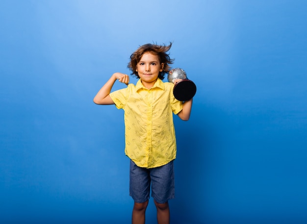 Menino estudante estudante de 7 anos com um globo de lembrança nas mãos sorrindo sobre um fundo azul