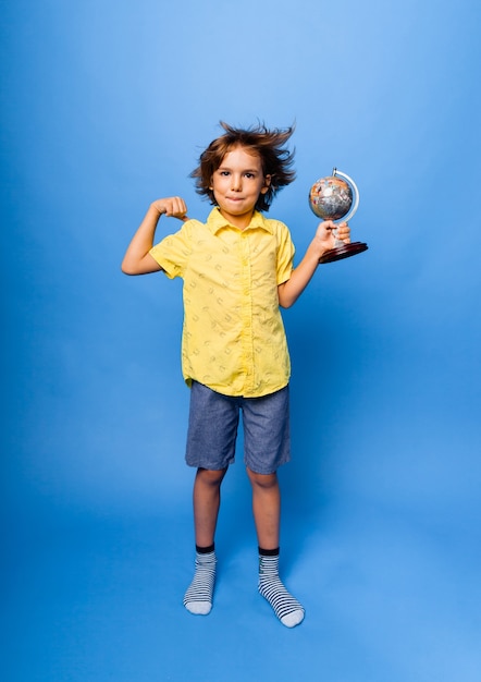 Foto menino estudante estudante de 7 anos com um globo de lembrança nas mãos sorrindo sobre um fundo azul