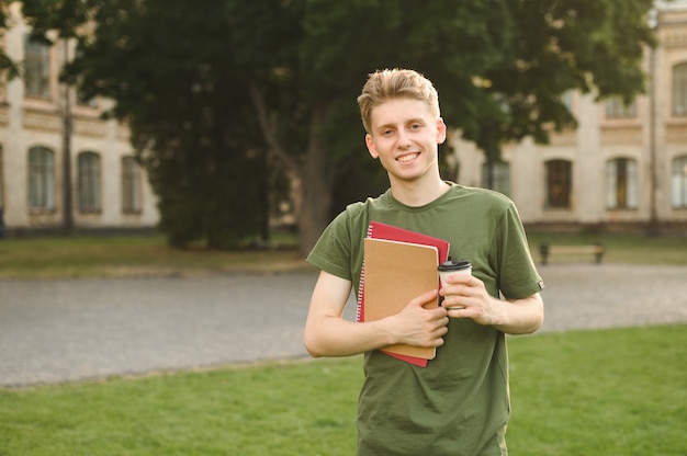 Menino estudante universitário sorridente e positivo perto do campus com livros