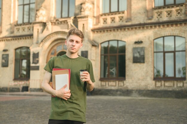 Menino estudante universitário sorridente e positivo perto do campus com livros