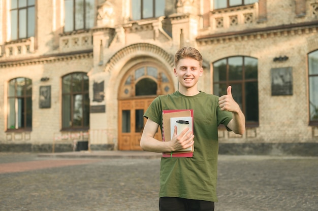 Menino estudante universitário sorridente e positivo perto do campus com livros