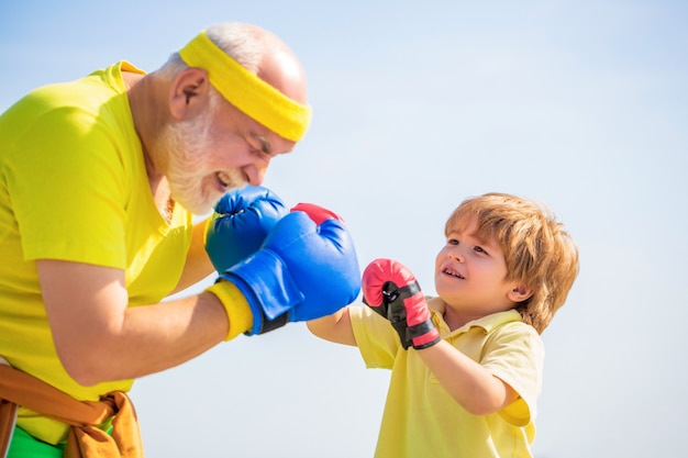 Menino fazendo exercício de boxe com o avô. Pai está treinando seu filho boxe. Desportista de menino em treinamento de boxe com o treinador. Esportes homem treinador de boxe garotinho em luvas de boxe vermelhas.