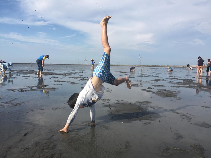 Foto menino fazendo handstand na praia contra o céu durante o pôr do sol
