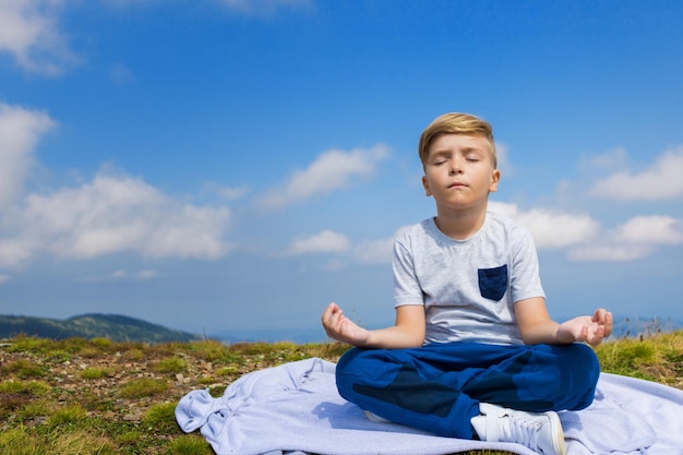 Menino fazendo ioga na montanha contra o céu azul