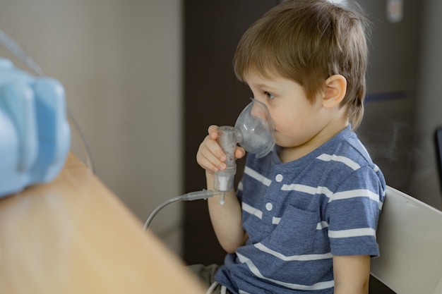 Foto menino fazendo terapia de inalação respiratória com nebulizador enquanto assiste desenhos ao telefone