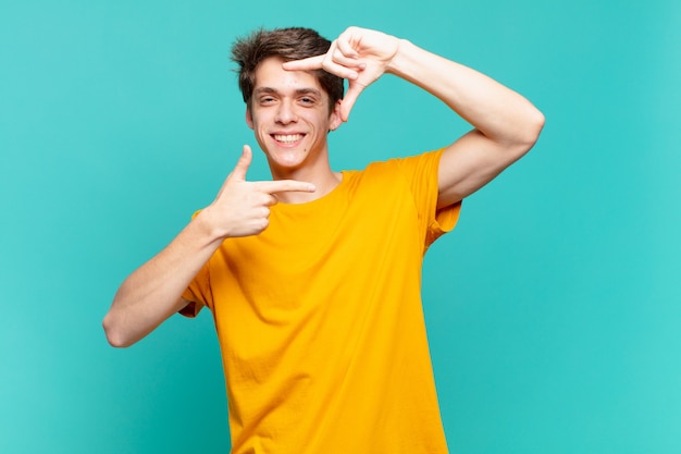 Menino feliz, amigável e positivo, sorrindo e fazendo um retrato ou moldura com as mãos