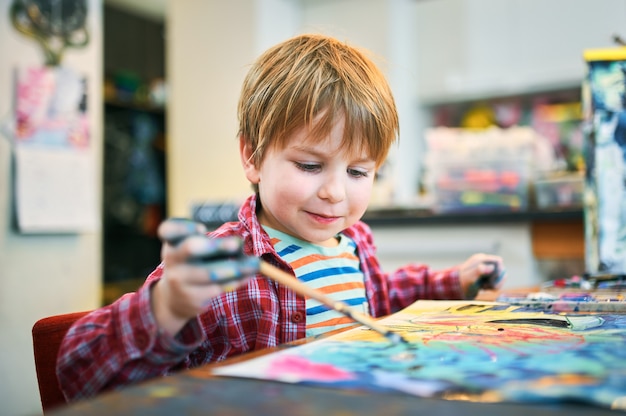 Menino feliz bonitinho, criança em idade pré-escolar adorável, pintando em um estúdio de arte ensolarado.