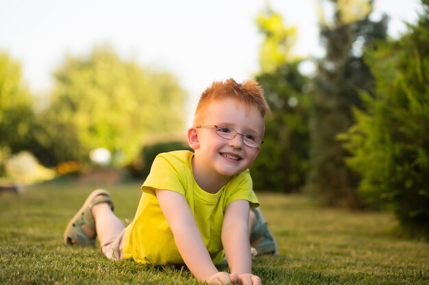 Menino feliz com cabelo ruivo de óculos na grama