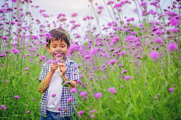 Foto menino feliz com explorador de lupa e aprendendo a natureza, jardim de flores no quintal