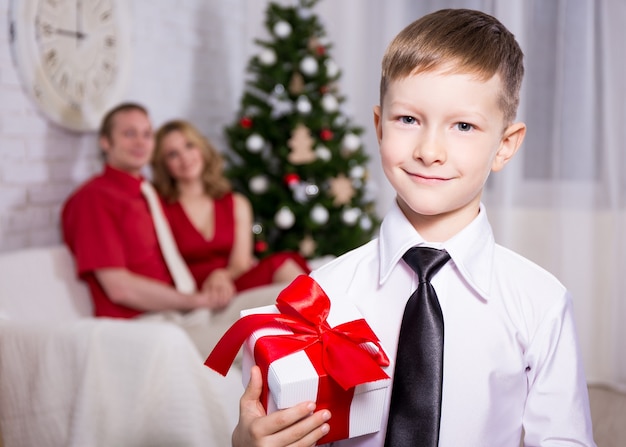 Menino feliz com um presente de seus pais e a árvore de natal