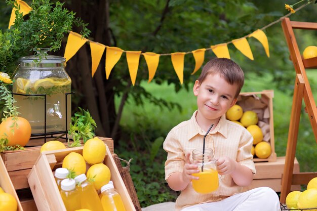 Menino feliz comendo limões e bebendo limonada ao ar livre no verão