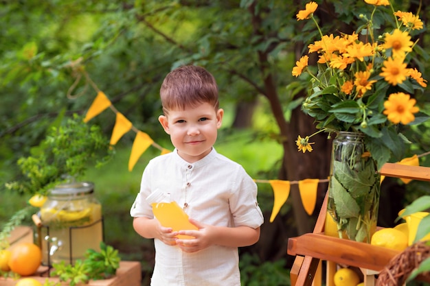 Menino feliz comendo limões e bebendo limonada ao ar livre no verão