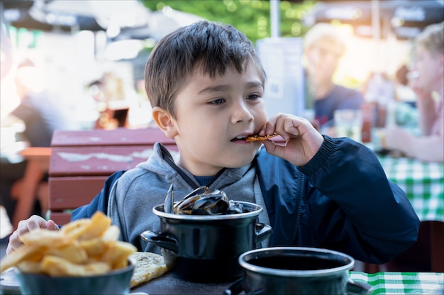 Menino feliz comendo pele de porco crocante e mexilhões frescos cozidos no vapor com alho