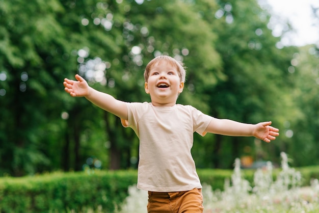 Menino feliz corre com os braços estendidos pelo parque no verão