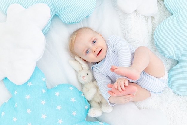 Menino feliz de seis meses deitado na cama com um coelhinho de pelúcia, lindo bebê loiro