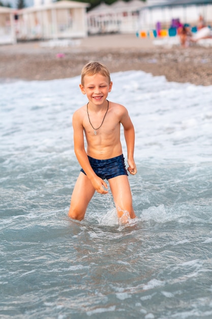 Menino feliz e ativo se divertindo nas ondas à beira-mar