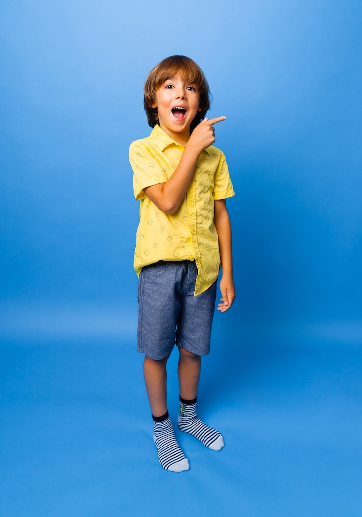 Foto menino feliz e emocional surpreso, mostra algo com o dedo no fundo azul