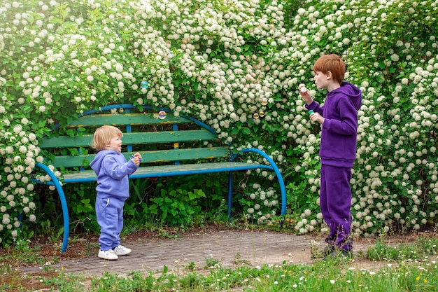 Foto menino feliz e seu irmão em um parque gostando de fazer bolhas de sabão. conceito de amizade de infância feliz