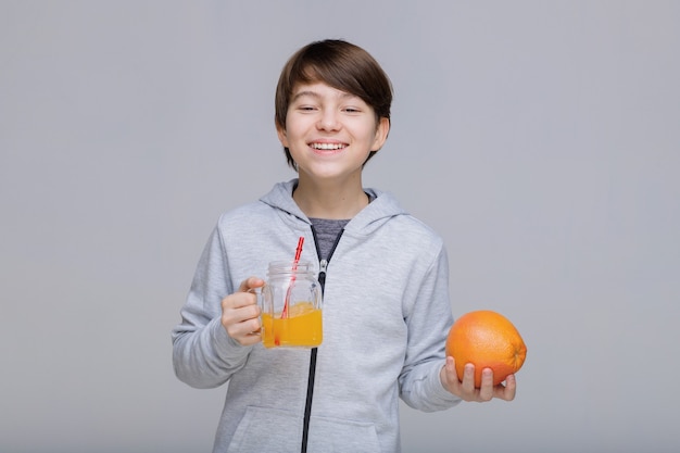 Menino feliz e sorridente bebendo suco fresco de um copo com um canudo