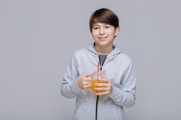 Menino feliz e sorridente bebendo suco fresco de um copo com um canudo