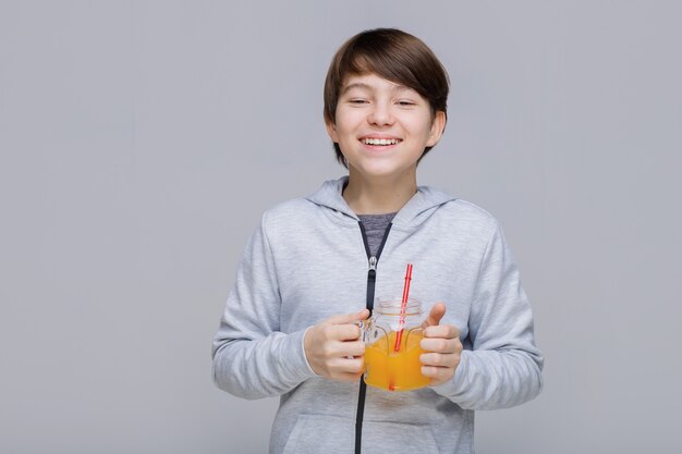 Menino feliz e sorridente bebendo suco fresco de um copo com um canudo