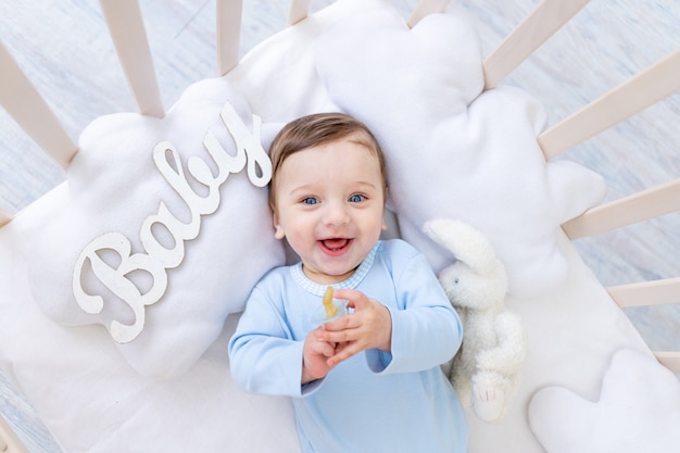 Menino feliz e sorridente no berço com a inscrição do bebê em um macacão azul, um bebezinho fofo e alegre no quarto