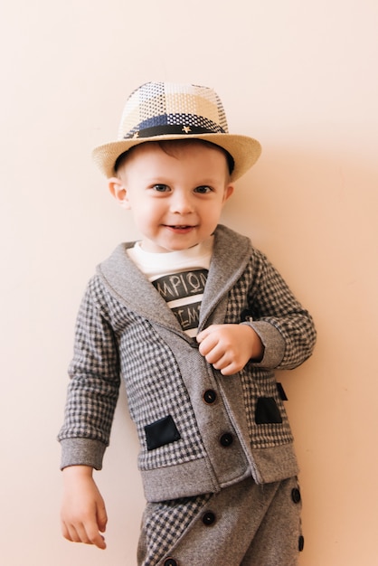 Foto menino feliz em terno cinza, chapéu na parede de luz